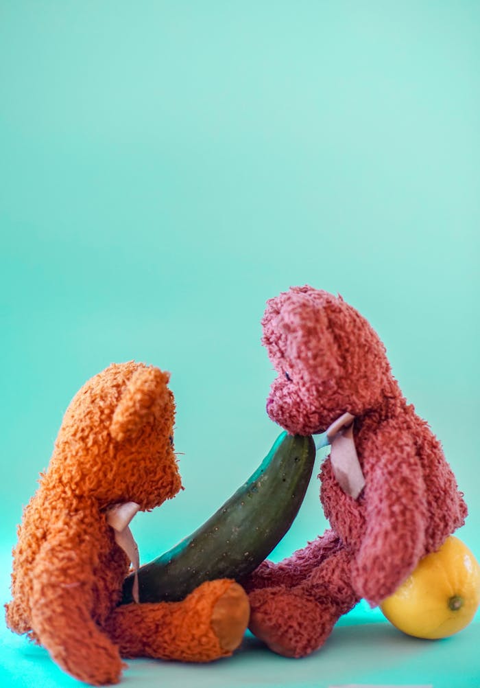 Two colorful teddy bears interacting creatively with fruits and cucumber.